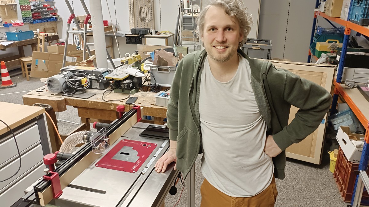 Henning looks very pleased at the camera. He rests his hand on the freshly assembled milling table in the wood workshop.